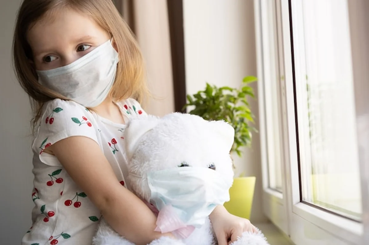 Smutne dziecko i pluszowy miś w maseczkach medycznych na parapecie