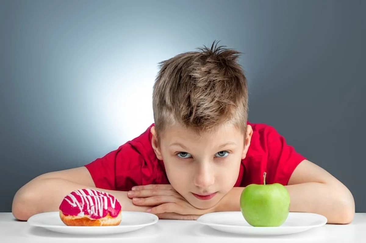 Chłopiec wybiera między pączkiem a zielonym jabłkiem