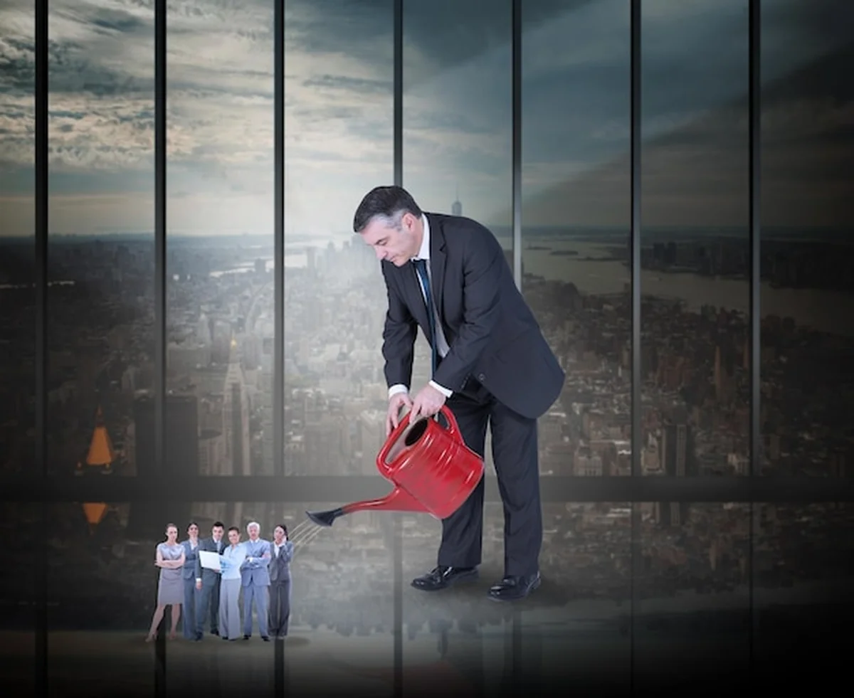 Dojrzały biznesmen podlewa malutki zespół biznesowy przed dużym oknem z widokiem na miasto