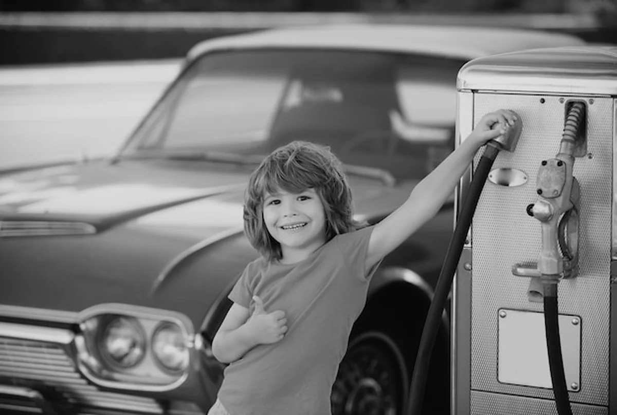 Dziecko przed czerwonym samochodem retro na stacji benzynowej