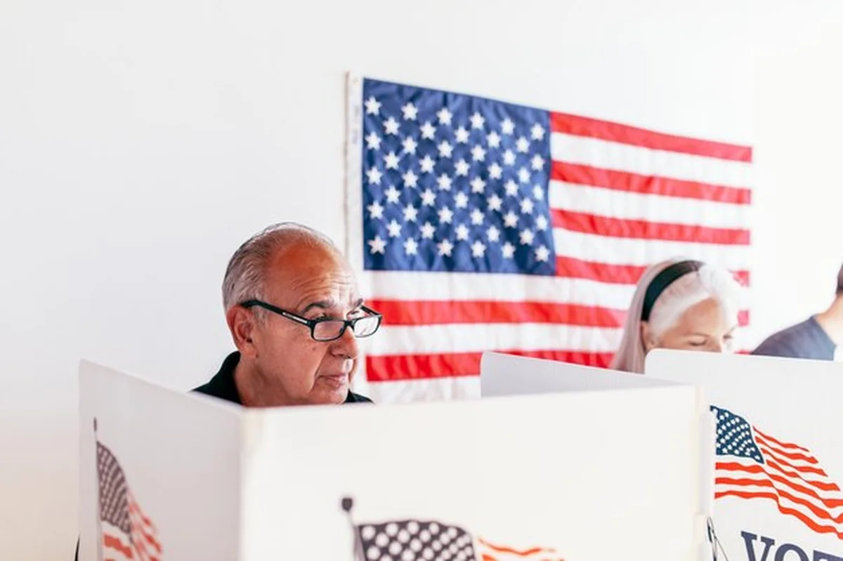 Starszy mężczyzna głosuje w kabinie z flagą amerykańską