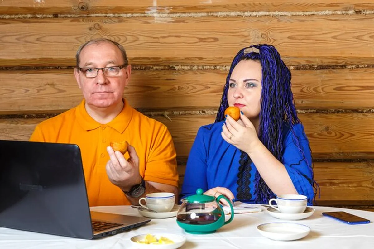 Małżeństwo przy stole pije herbatę i pracuje przy komputerze