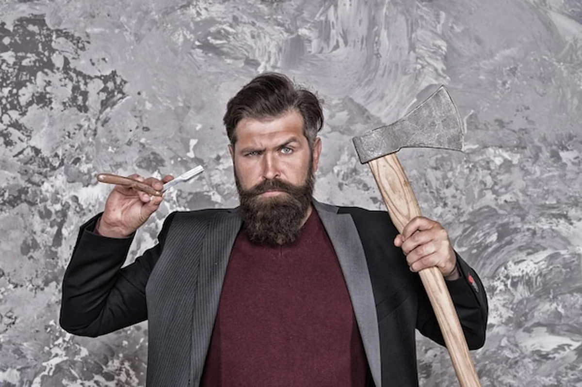 Hipster trzyma brzytwę i siekierę, przygotowania do golenia w salonie fryzjerskim