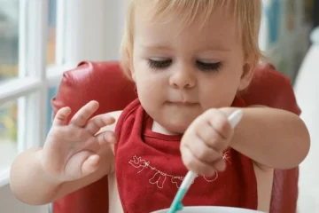 Niemowlę jedzące owsiankę na wysokim krześle