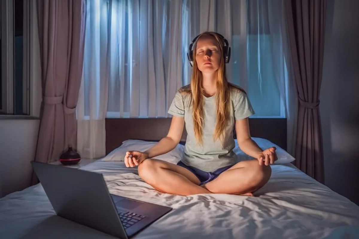 Kobieta medytuje w łóżku z aplikacją medytacyjną