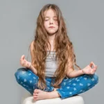 Mała dziewczynka medytuje w pozycji lotosu na szarym tle