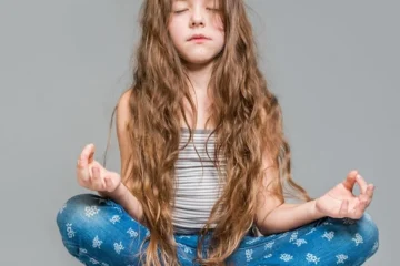 Mała dziewczynka medytuje w pozycji lotosu na szarym tle