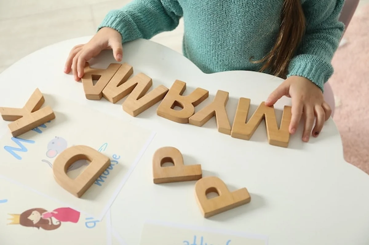 Mała dziewczynka uczy się alfabetu drewnianymi literami przy białym stole
