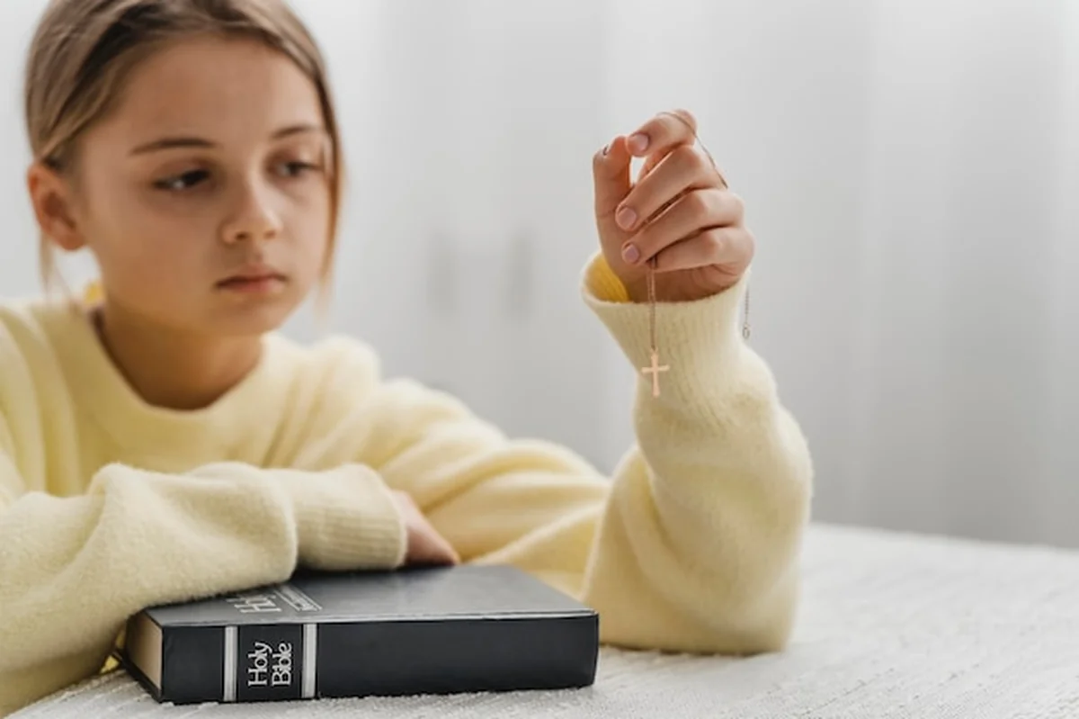 Dziewczynka modli się w domu z Biblią i krzyżem na szyi