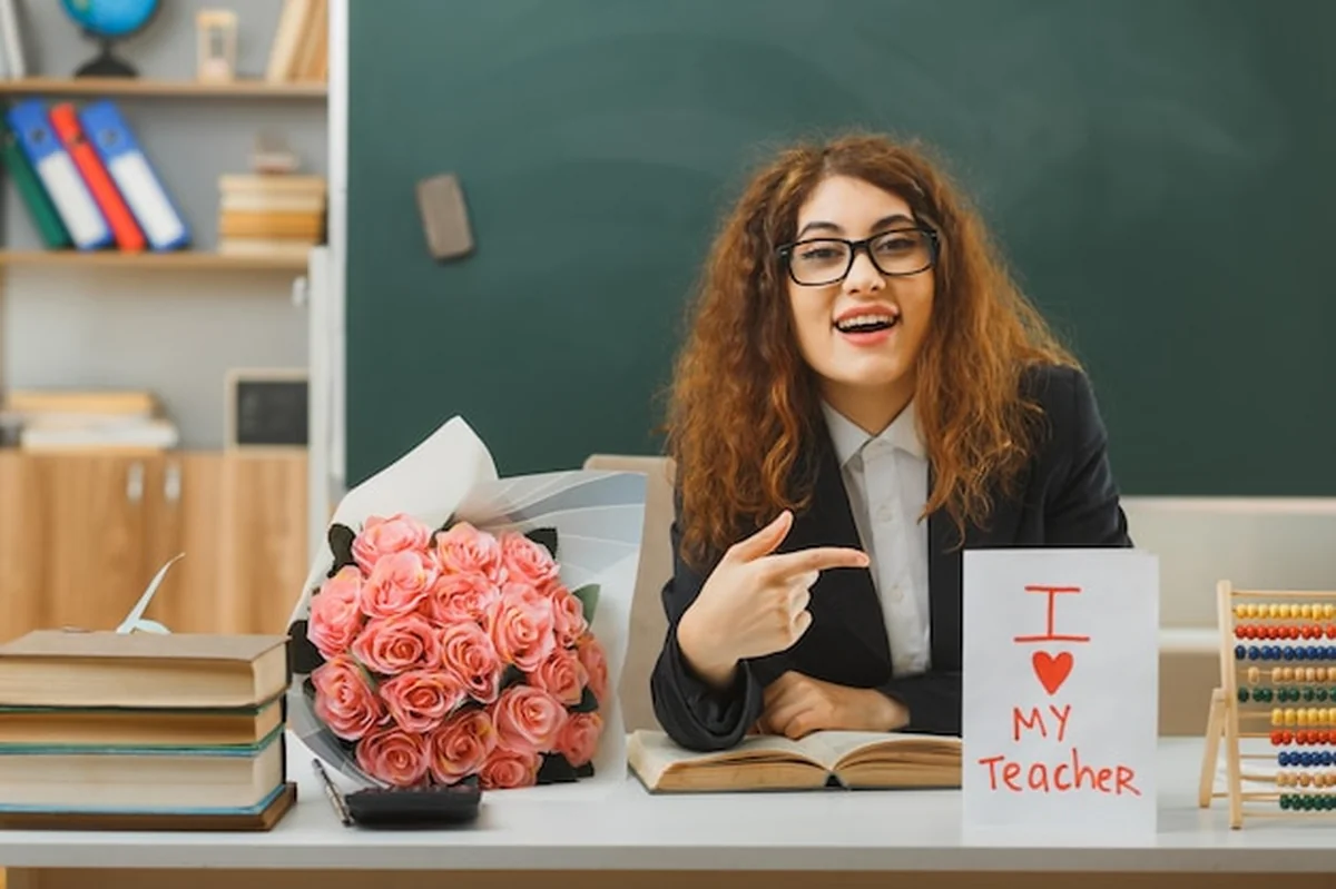 Młoda nauczycielka przy biurku ze szkolnymi narzędziami w klasie