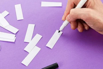 Pisanie ręką na małych białych paskach papieru czarnym markerem na fioletowym tle